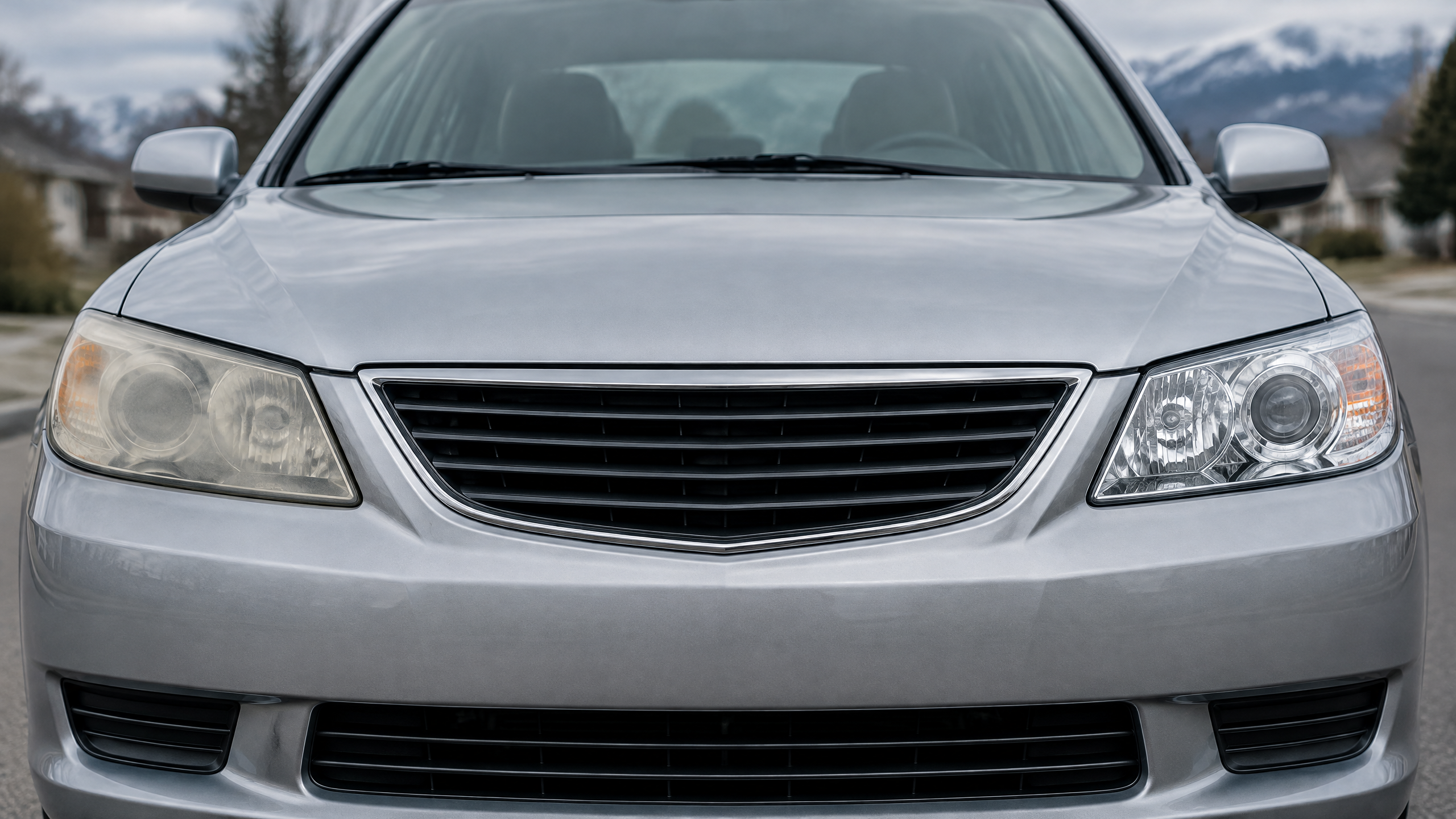 Unbranded silver vehicle with the left exterior headlight lens more cloudy than the clearer right lens