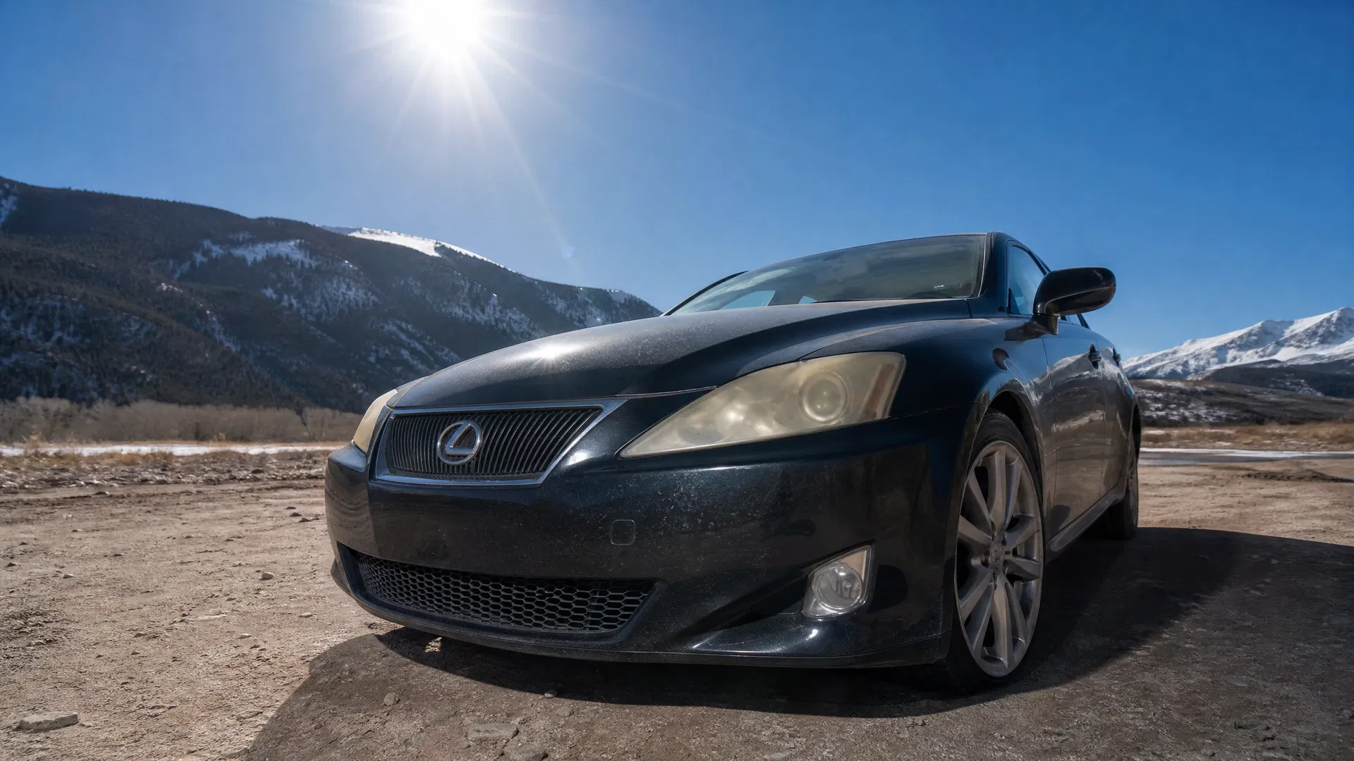 Car with yellowed hazy headlights parked under the intense Colorado sun with the Rocky Mountains visible in the background